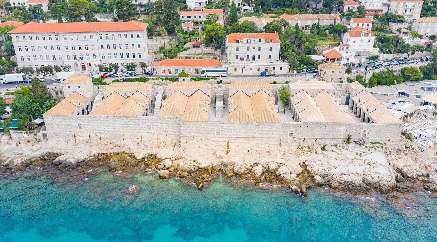 Lazareti-komplekset set fra oven, en lang stenbygning med tegltage langs det turkisblå Adriaterhav, med Dubrovniks skråninger i baggrunden.